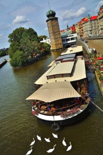 Floating restaurant on vltava river in prague with white swans swimming nearby and the medieval