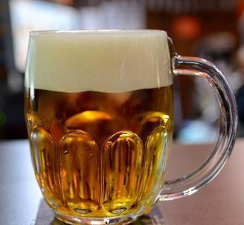 Large glass mug full of cold, golden beer with a thick head, creating a refreshing scene in a pub,