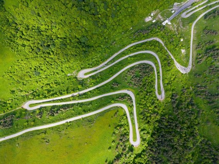 Aerial view of a serpentine road winding through a green, wooded landscape, aerial view, road H52