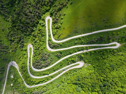 Serpentine road winding through green hills and forests, aerial view, road H52 above a tunnel,