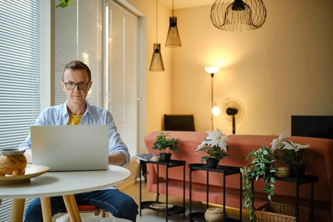 A man is focused on his laptop while seated at a small round table in a stylish living room