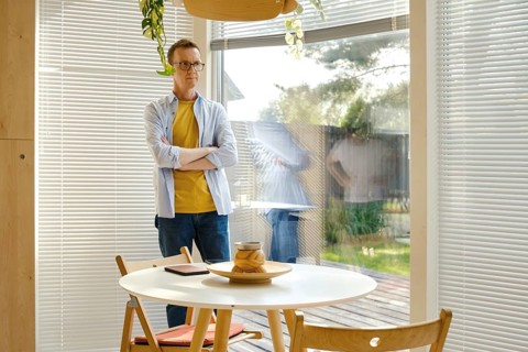 A middle-aged man with glasses stands with crossed arms beside a round table in a well-lit, modern