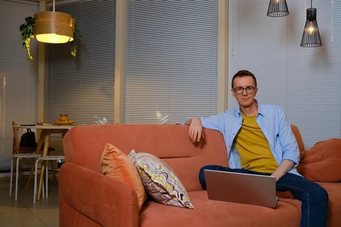 A man sits comfortably on a coral sofa, focused on his laptop in a cozy living room decorated with