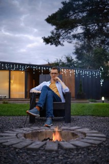 A person sits comfortably in a chair by a fire pit, enjoying a quiet evening outdoors. The setting