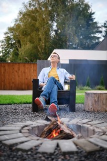 A middle-aged man enjoys a tranquil warm evening in his backyard, sitting in a wooden chair next to