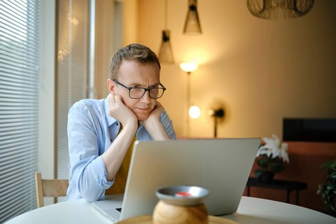 A middle-aged man with glasses watching series on his laptop while seated at a round table in a