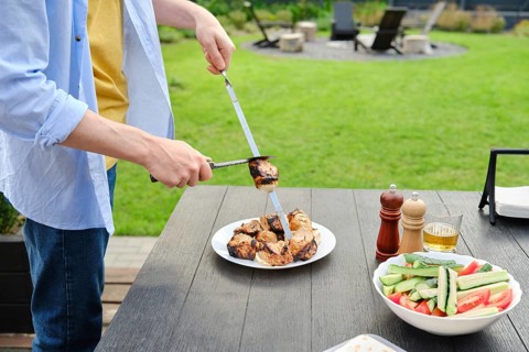 Unrecognizable man removes grilled meat from skewer to a plate. The concept of a picnic in the