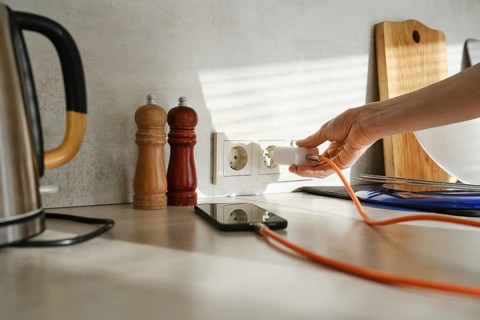 A person plugs a smartphone charger into an outlet while standing in a stylish kitchen