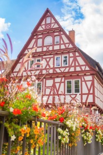Half-timbered house with lush floral decorations under a clear sky conveys a summery atmosphere,