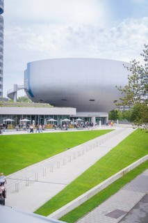 Large modern building surrounded by a green park with people out for a walk, BMW Welt, Munich,