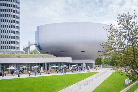 Futuristic-looking building with many visitors and manicured green space in the foreground, BMW