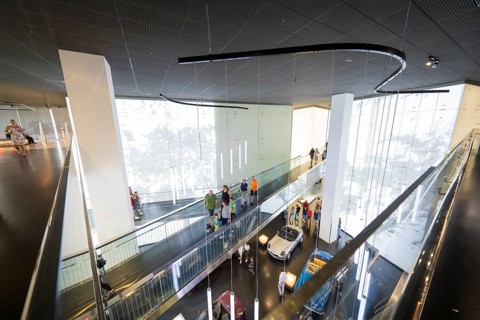 Modern interior with group of visitors and exhibited vehicles under dynamic light installations,