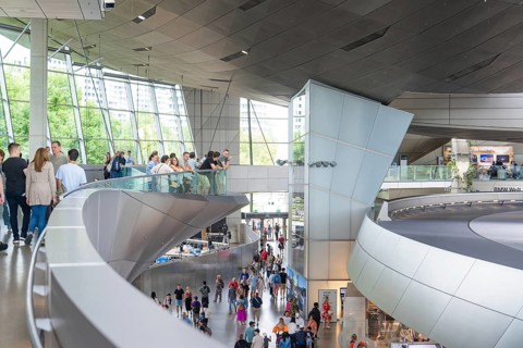 People in a corridor with a view of a glass front and modern architectural features, BMW Welt,