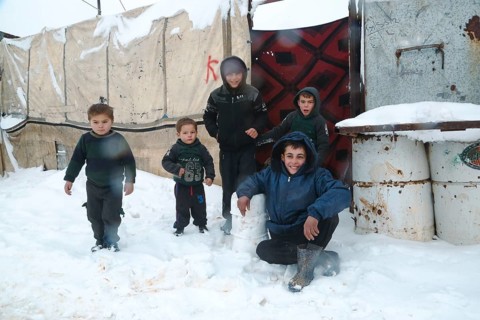 Displaced Syrian children playing in the snow near their tents inside a refugee camp during winter.