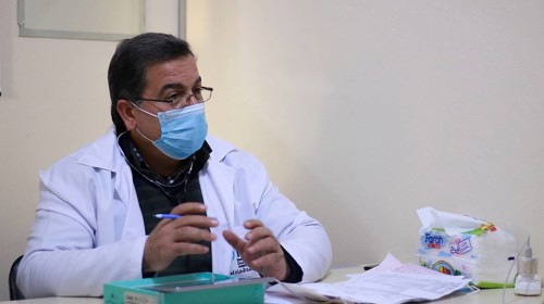 A Syrian doctor wearing a protective mask consults with a displaced patient inside a medical clinic