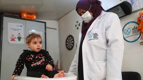A doctor examining a refugee child for malnutrition in the camp using weight and height measurement