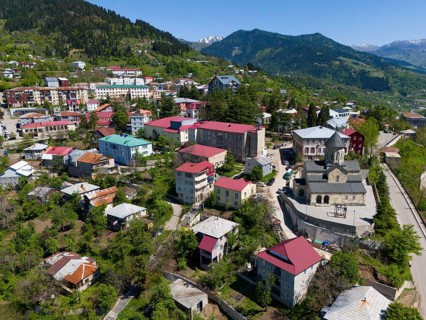 Small town with colourful houses and church, surrounded by green mountains under a clear sky,