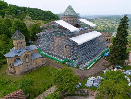 Large church with scaffolding on a hill in a green landscape, aerial view, Gelati Monastery near