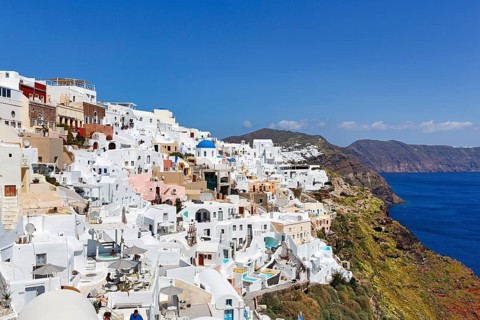 White and colourfully painted holiday homes, orthodox church with blue dome on the edge of the