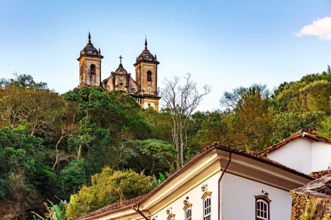 Historic buildings and a baroque church amidst the vegetation of the hills of the city of Ouro