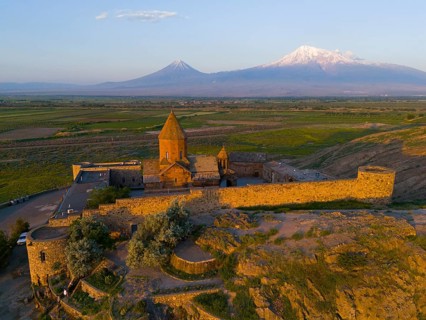 An old church surrounded by walls in front of a mountain range at dawn, aerial view, Chor Wirap