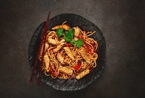 Udon noodles, with squid and vegetables, on a black plate, homemade, no people