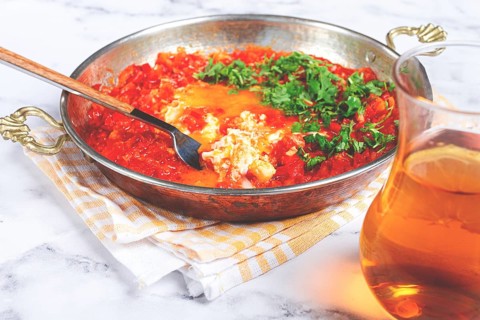 Traditional Turkish dish, scrambled eggs with tomatoes, Menemen, with herbs, in a frying pan,