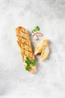 Garlic bread, baguette with garlic butter and herbs, on a light table, top view