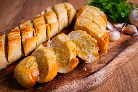Garlic bread, baguette with garlic butter and herbs, on a wooden board, with herbs and garlic