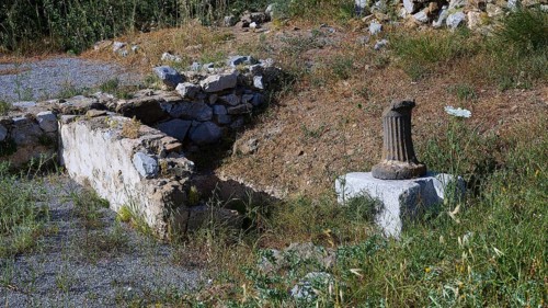 An old wall and a column surrounded by grass and flowers, ancient Roman bath, Tallaras, Analipsi,