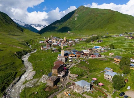 Village with river course, surrounded by green mountains and meadows under a blue sky and striking