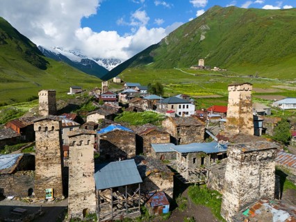 Historic towers and buildings in a winding mountain valley with green meadows and stone structures,