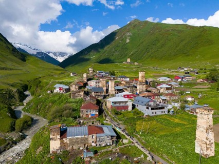 A picturesque mountain village with historic towers and green hills under a blue sky, aerial view,