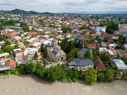 Close-up of a city view with a central church, residential houses and a river next to wooded hills,