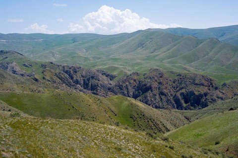 Green hills with clouds in the sky and a gorge depicting a peaceful landscape, view of the