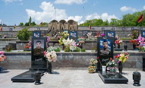 Row of decorated tombstones with portraits and flowers, Armenian flag visible, graves of 2020,