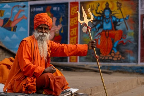 Indian sadhu holding trident, with image of Shiva in the background, Bangali Tola, Varanasi, Uttar