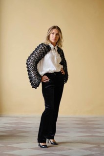 A middle-aged woman stands with hands on her hips in a trendy outfit featuring a unique sweater and