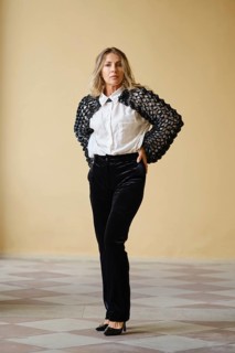 A middle-aged woman stands confidently with her hands on her hips, wearing a fashionable black and