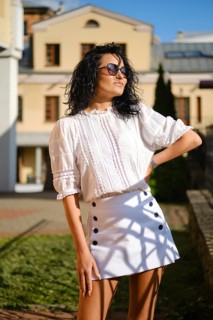 Bright sunlight highlights a woman posing confidently in a chic white blouse and skirt. She stands