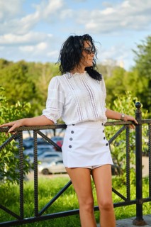 In a vibrant park setting, a woman poses confidently in a white blouse and mini skirt. Sunlight