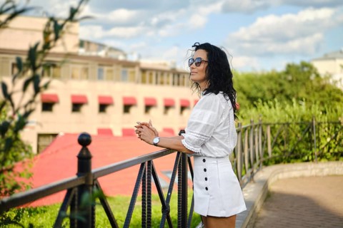 A woman stands casually leaning against a decorative railing, gazing thoughtfully at the cityscape.