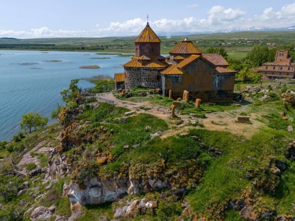 Church on a rocky outcrop, surrounded by lush greenery, overlooking a tranquil lake, aerial view,
