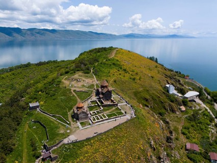 Panorama of a monastery on a green hill with a view of a lake and mountains under a cloudy sky,