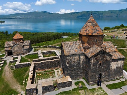 Historic stone monastery with a lake and mountain panorama under a cloudy sky, aerial view,