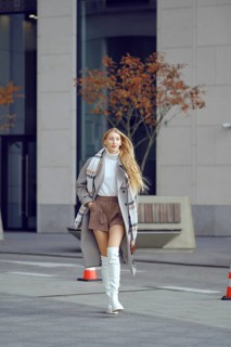 A confident woman strolls along a city street, wearing a trendy autumn outfit that includes boots