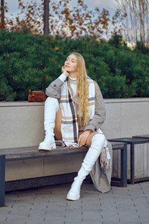 A dreamy woman sits thoughtfully on a bench in a park, dressed in a fashionable outfit with a long