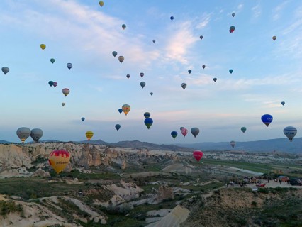Many colourful hot air balloons float over a vast Turkish landscape in the early morning, aerial