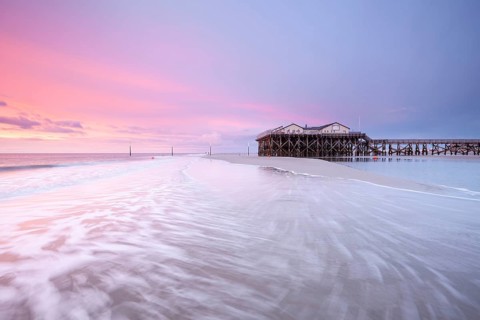 Pile dwellings in St. Peter-Ording in front of the surf in the bright red evening light by the sea