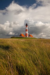 Illuminated Westerheversand lighthouse on the North Sea under dark storm clouds
